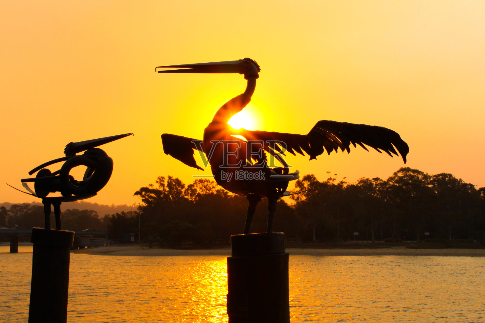 一个金属鹈鹕的剪影与金色的夕阳在小溪的背景照片摄影图片
