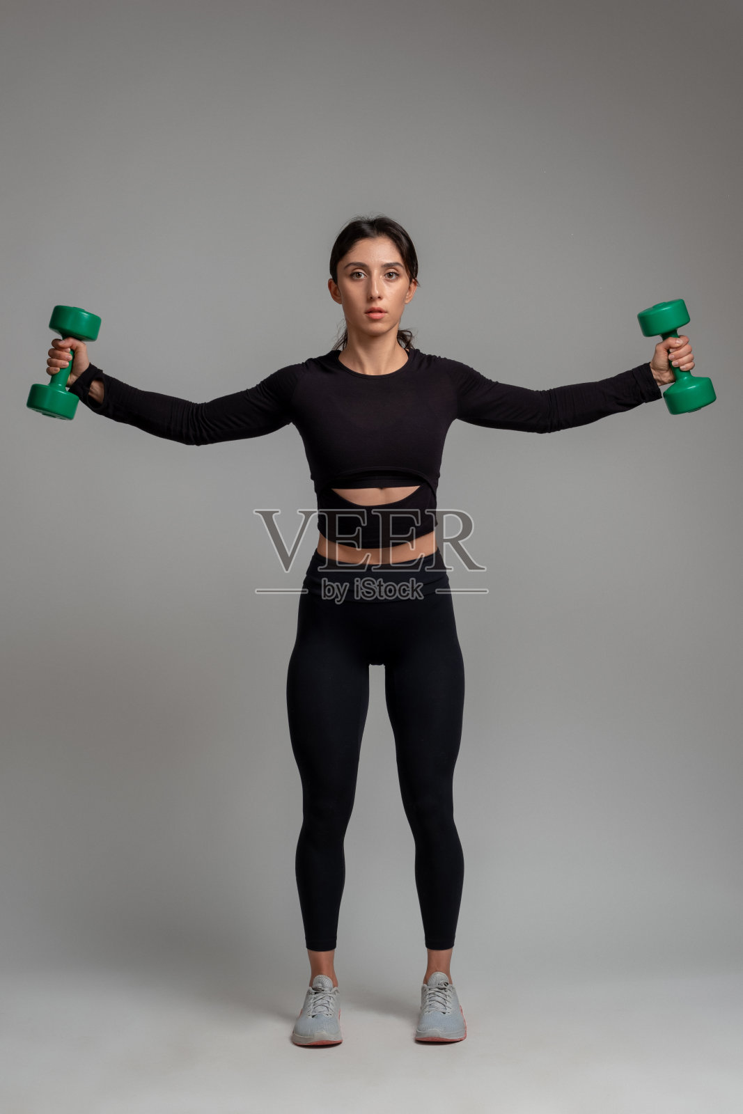 运动女孩在演播室用哑铃练习肩膀照片摄影图片