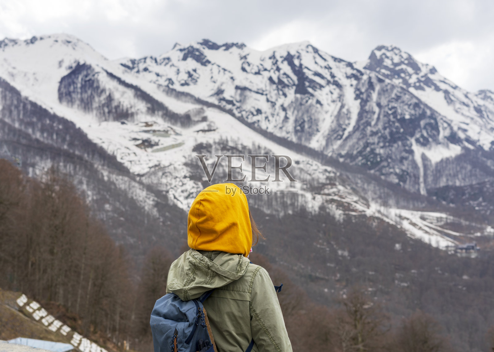 一个背着背包，戴着黄色头巾的年轻女子从后面欣赏白雪覆盖的高加索山峰照片摄影图片