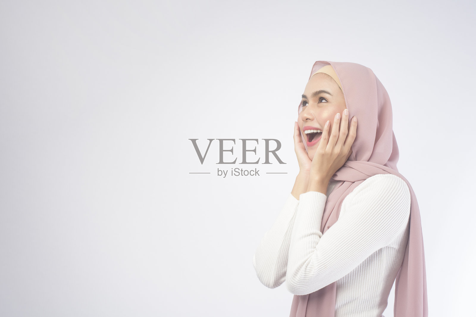 年轻微笑的穆斯林妇女的肖像戴着粉红色的头巾在白色的背景工作室。照片摄影图片