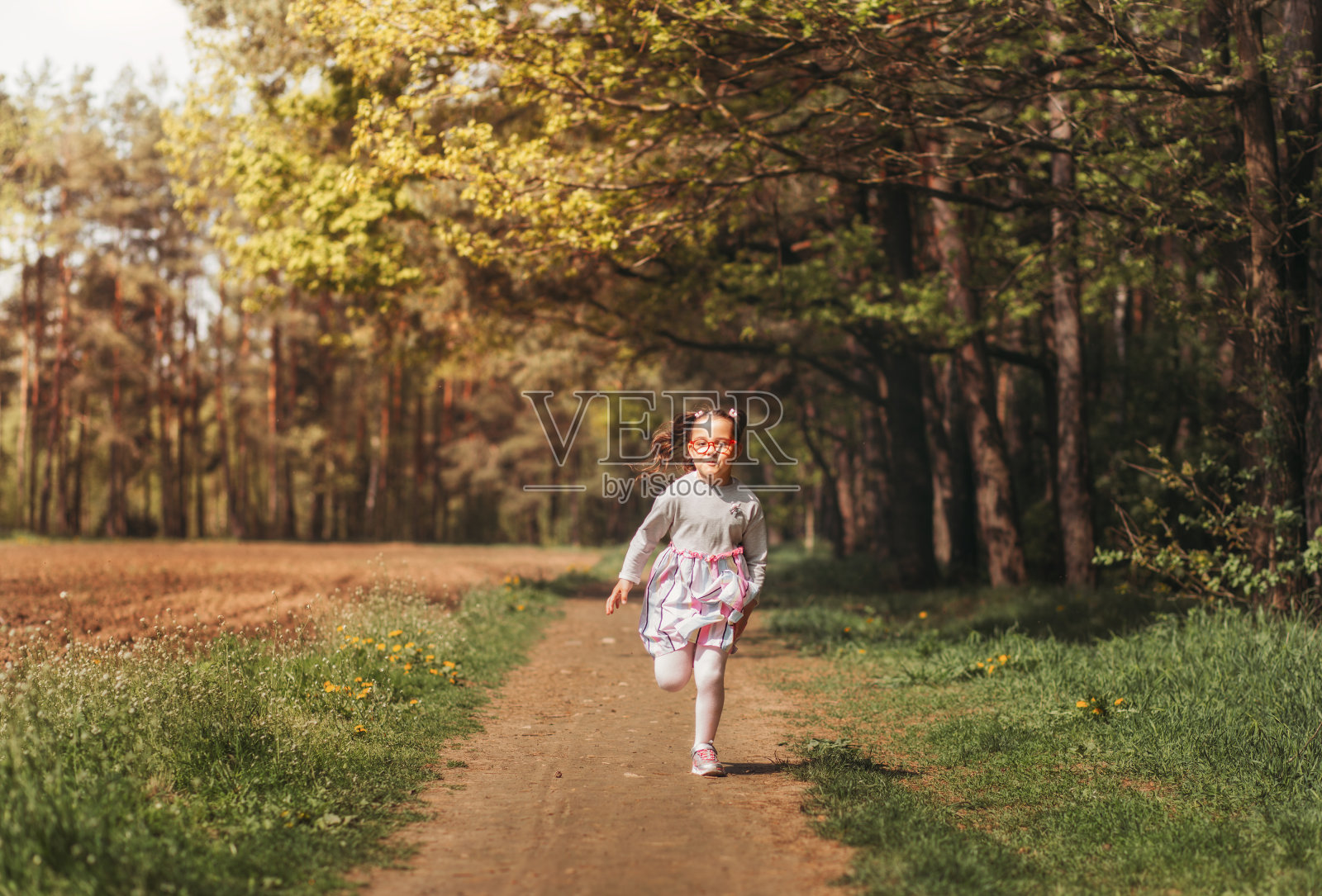 一个快乐的小女孩在夏天一个阳光明媚的日子里沿着一条森林小径奔跑照片摄影图片