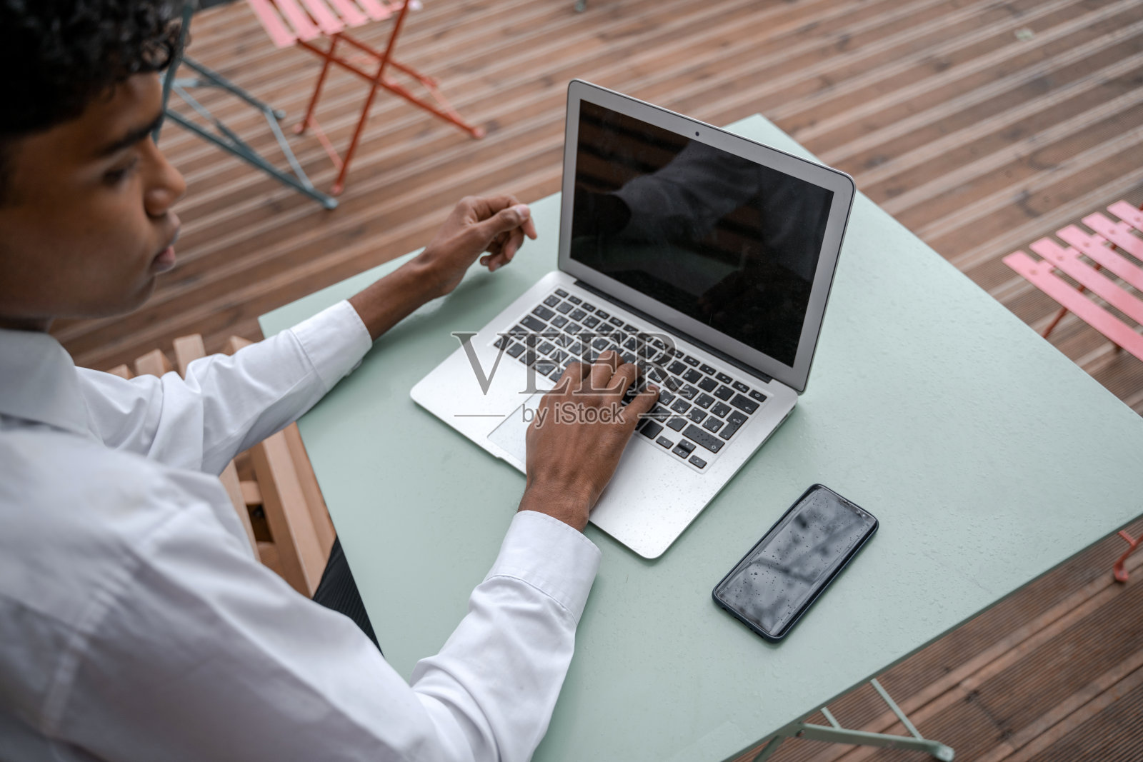 一个黑人年轻人工作场所的俯视图。在阳台上放智能手机和笔记本电脑。在办公室外工作，远程工作或学习的概念照片摄影图片