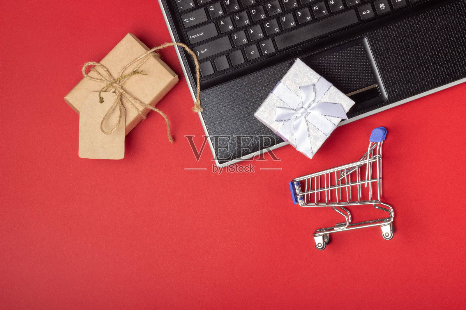 笔记本电脑，笔记本电脑，购物车和箱子在明亮的红色背景。网上购物的概念照片摄影图片