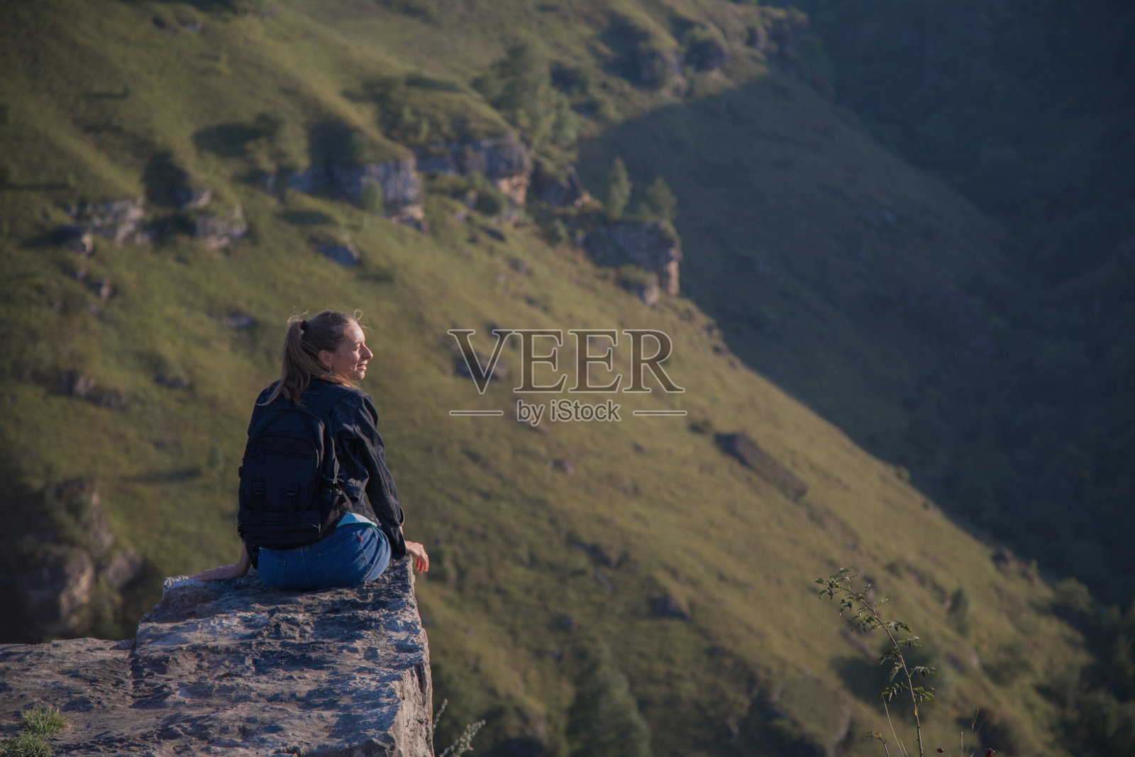 一个女孩背着背包站在悬崖边上。穿越高山之旅照片摄影图片