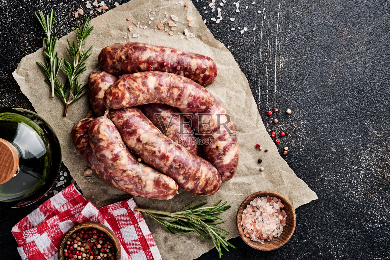 生香肠或烤肠放在羊皮纸和烹饪原料上。顶部视图与复制空间石桌。照片摄影图片