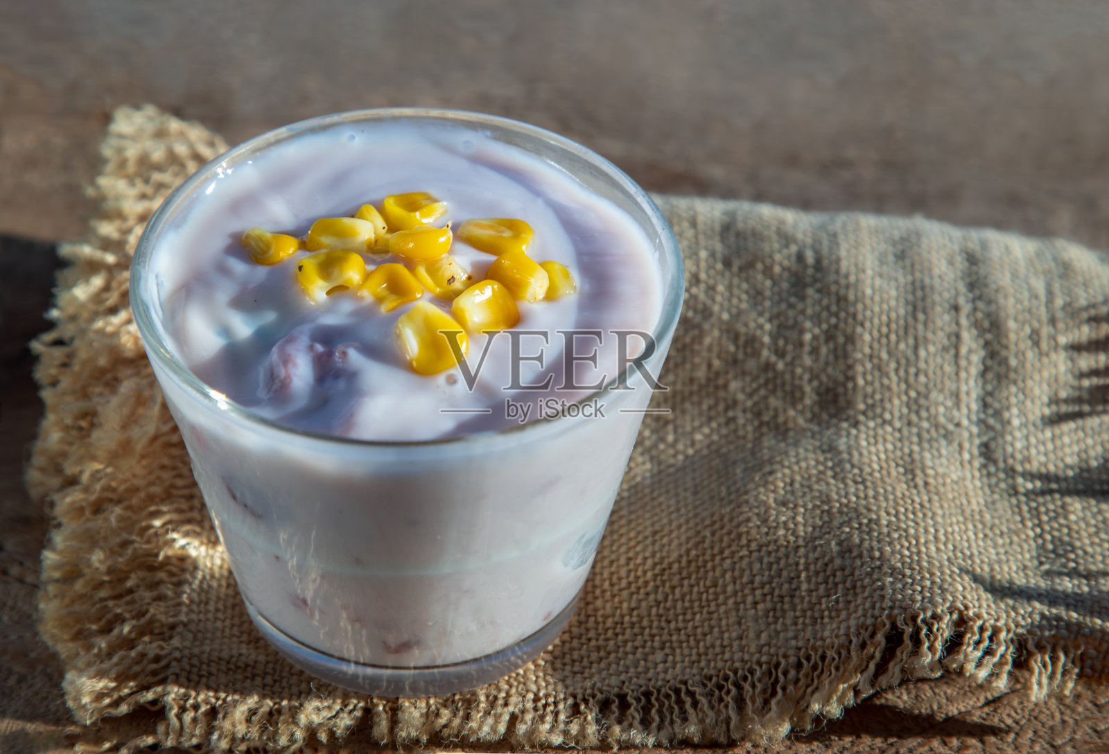 素食大豆草莓酸奶洒在玻璃上的成熟甜玉米粒在旧木桌上。照片摄影图片