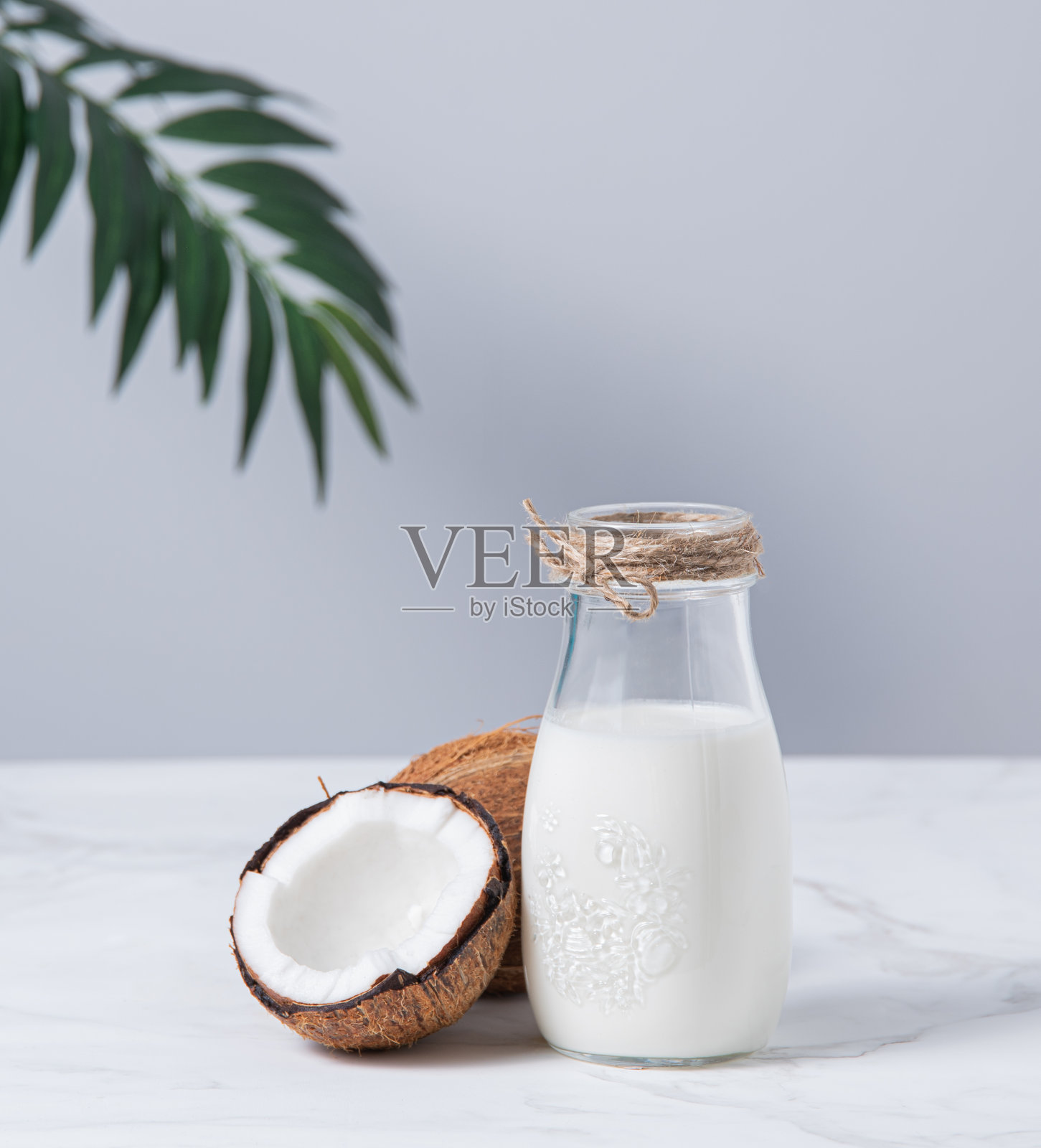 玻璃素食牛奶瓶放在白色大理石桌上，半椰子和棕榈枝。前视图和复制空间照片摄影图片
