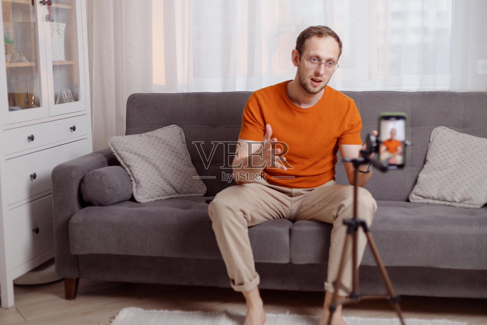 满脸胡须的中年男子用智能手机和三脚架在家直播照片摄影图片