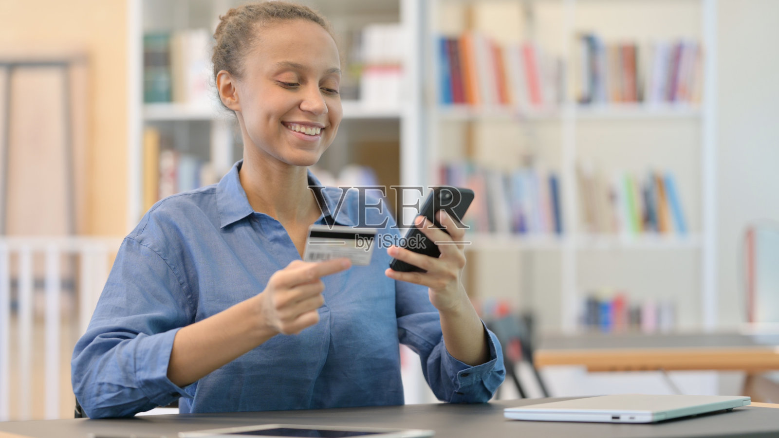 图书馆里的非洲妇女在智能手机上成功支付照片摄影图片
