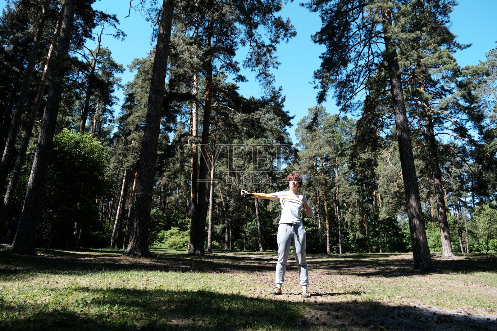 成熟的女人在松林里与阻力带一起锻炼照片摄影图片