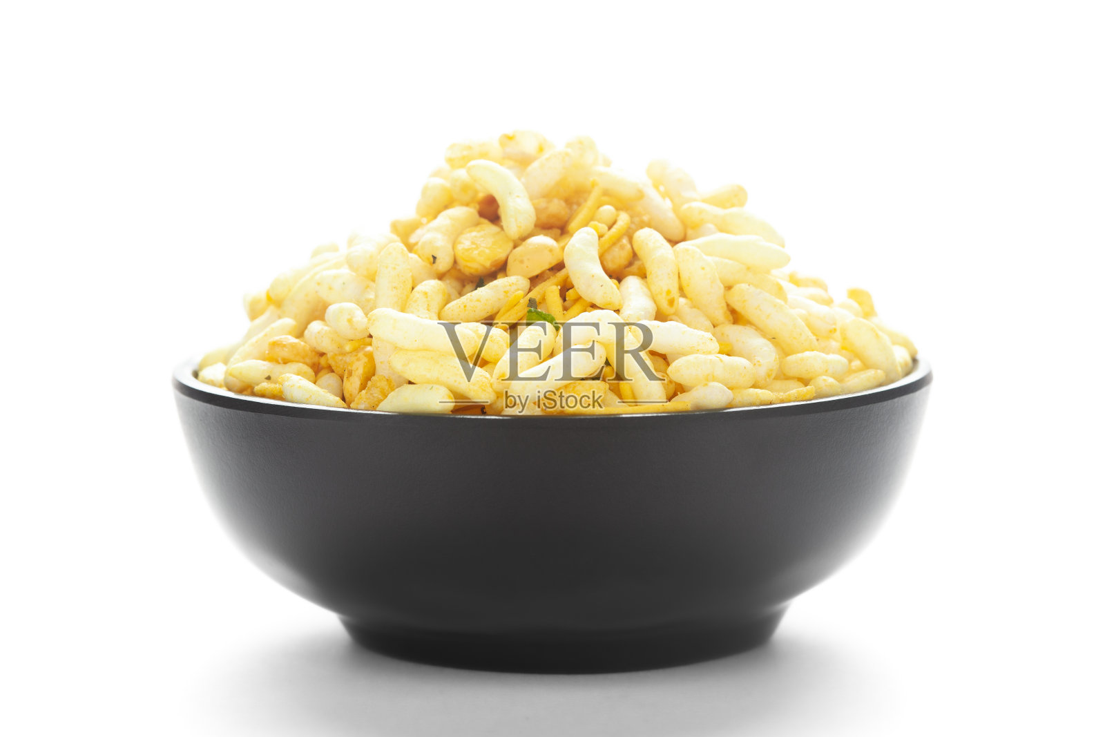 特写松脆Murmura在一个黑色陶瓷碗，与蓬松的米饭和咖喱叶。印度辣小吃(Namkeen)照片摄影图片