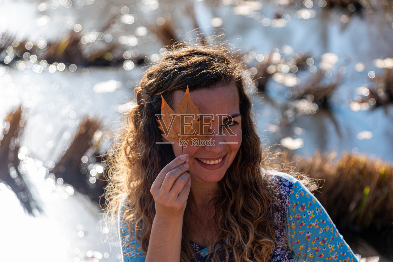 女人拿着一片枫叶，代表秋天的季节。季节照片摄影图片