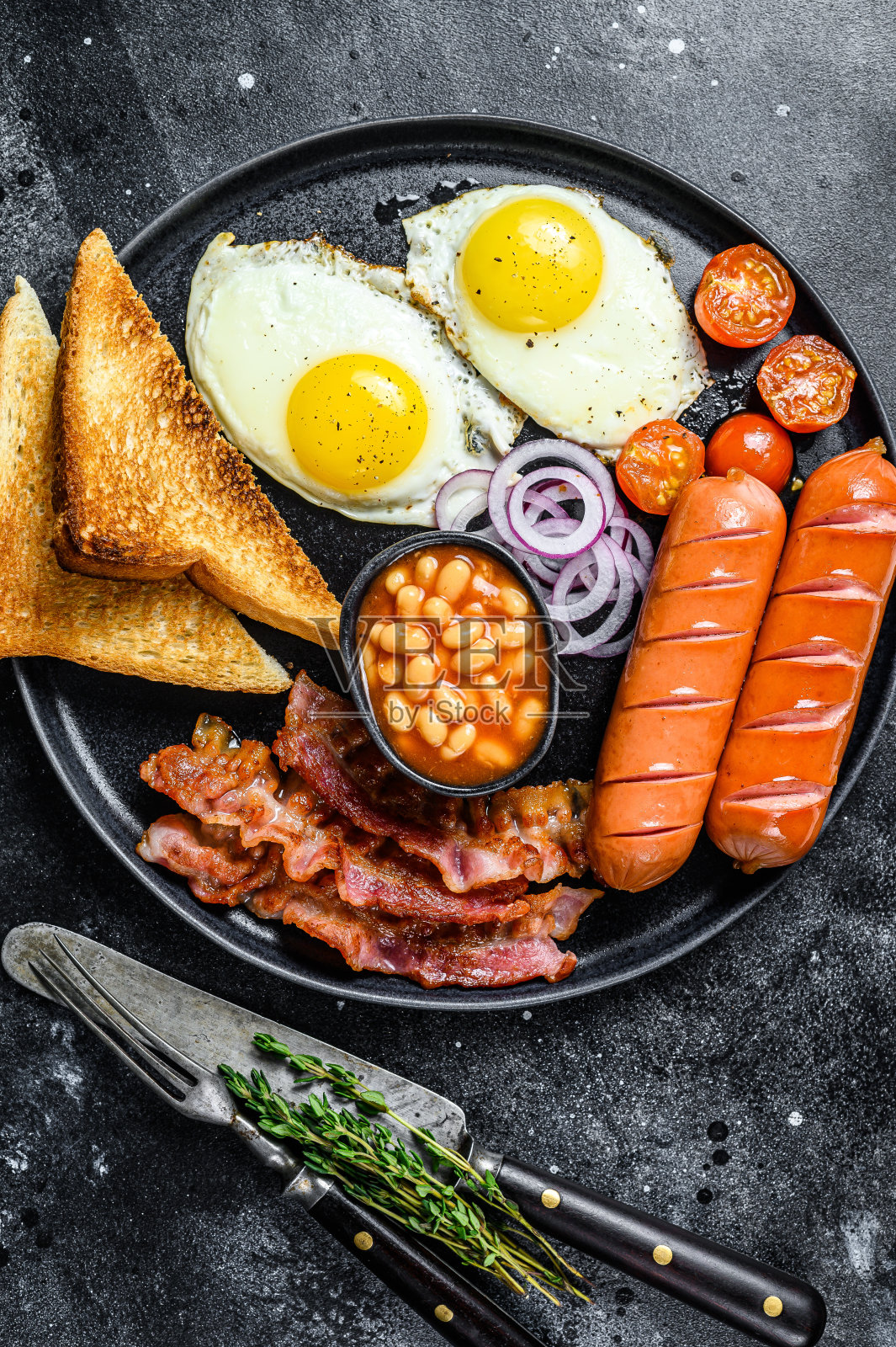 英式早餐，有煎蛋，香肠，培根，豆子和烤面包片。黑色背景。俯视图照片摄影图片