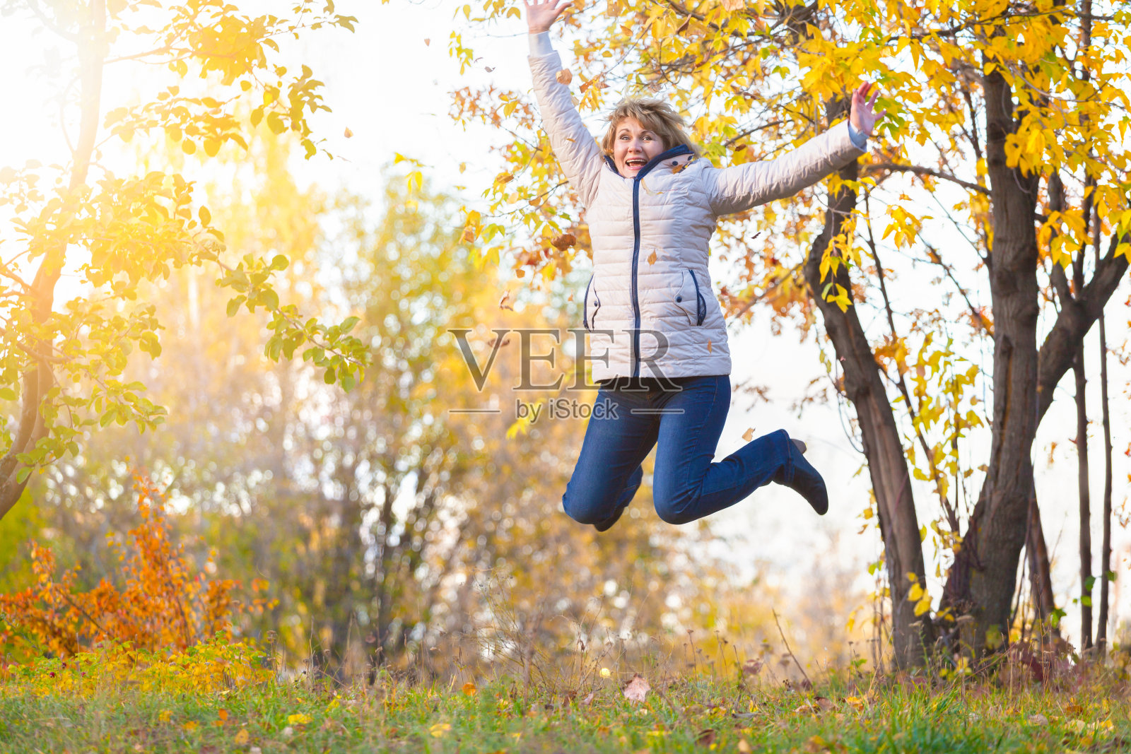 一位中年妇女在秋季公园的树林中散步。照片摄影图片