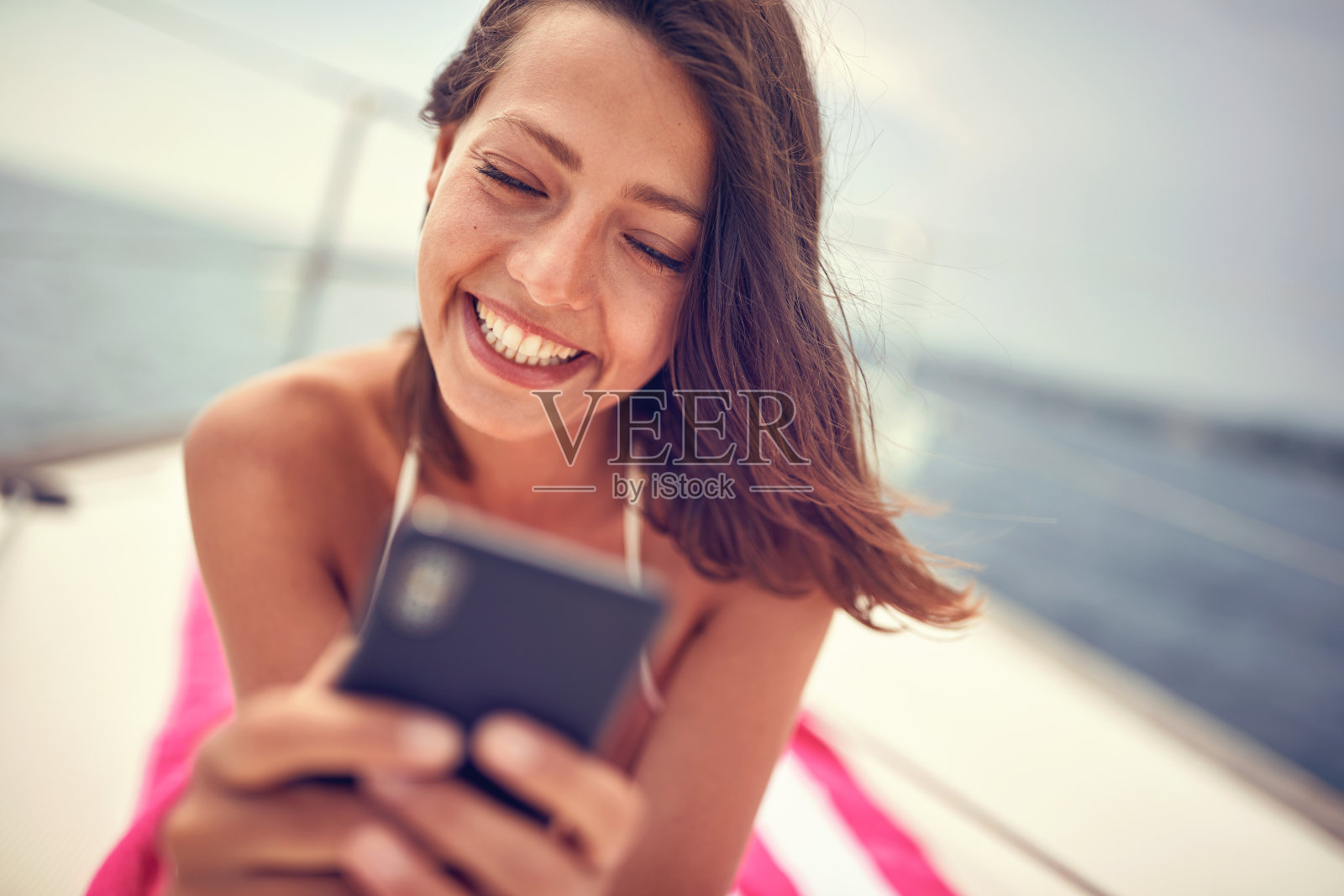 一个年轻性感的女孩的特写，她躺在毛巾上，在享受日光浴的时候聊智能手机。夏天,大海,假期照片摄影图片