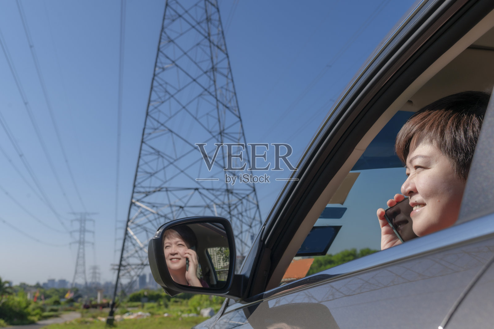 亚洲华人中年妇女坐在车内与手机交谈与窗户反射的电力线和天空照片摄影图片