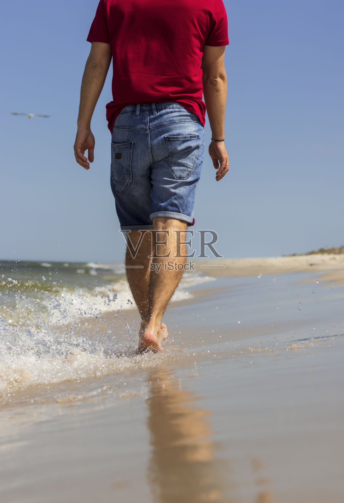 美丽的年轻男性沿着海滩漫步。照片摄影图片