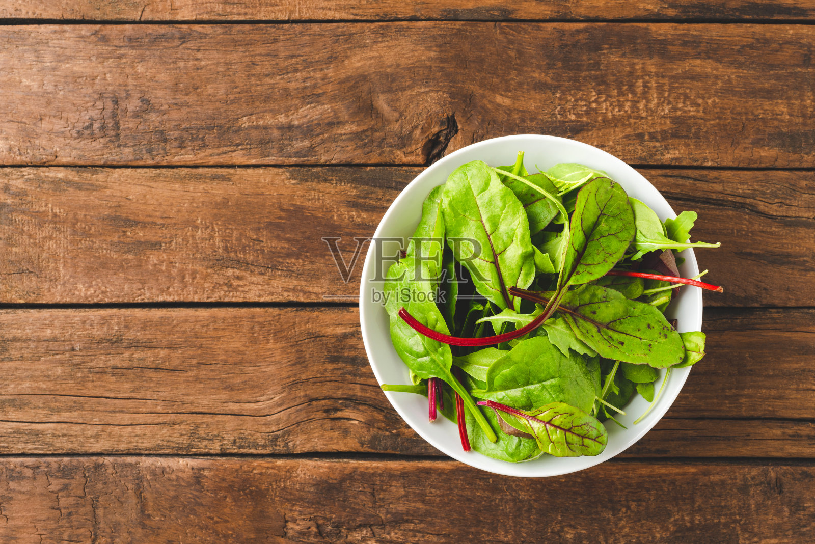 上方拍摄的新鲜蔬菜沙拉与菠菜，芝麻菜和甜菜根叶在碗里老木制背景与copyspace照片摄影图片