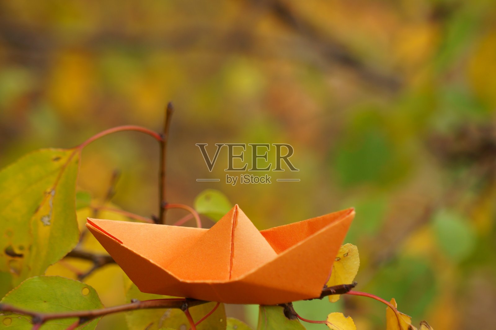 橙色的纸船在秋叶的背景上。照片摄影图片