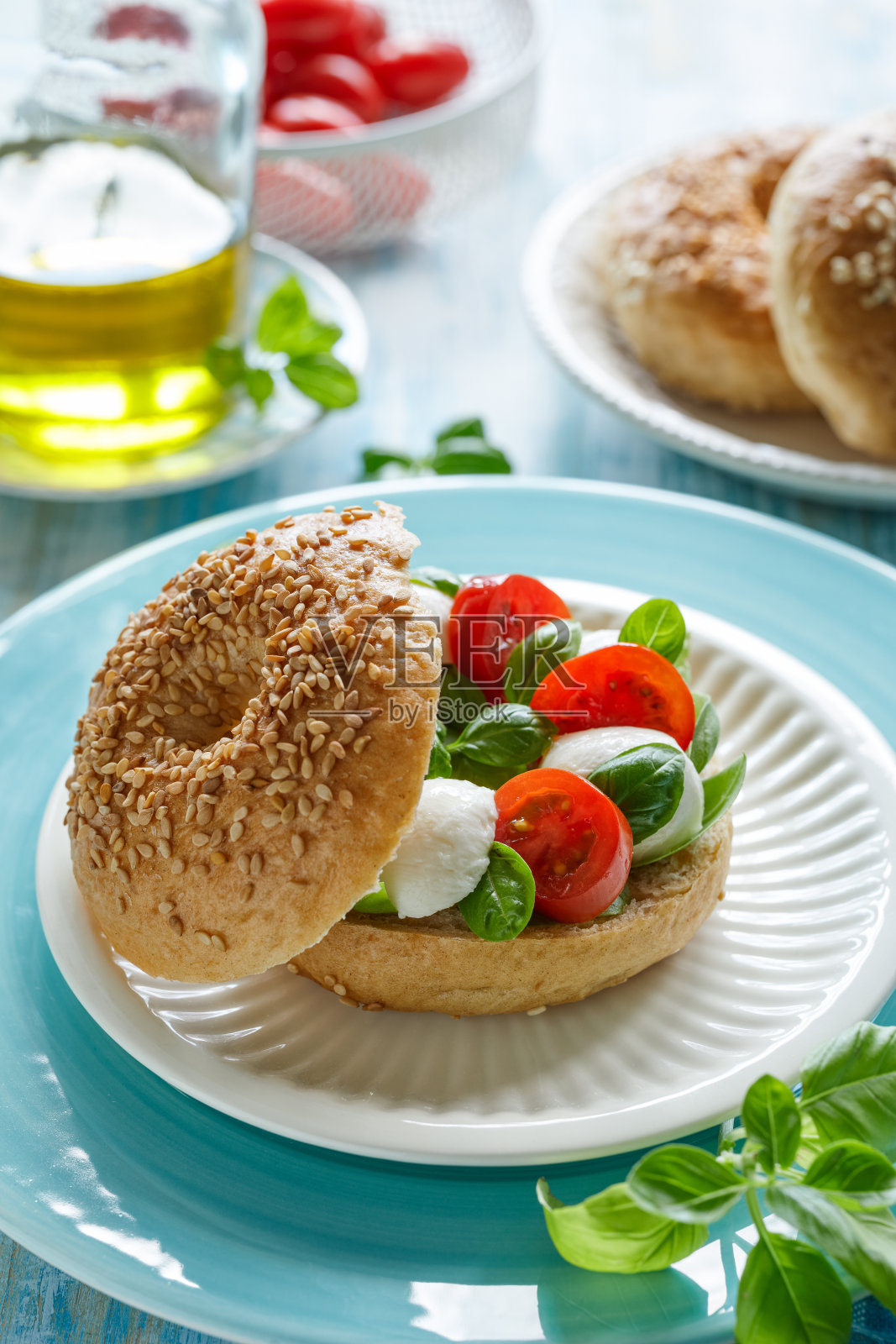 百吉饼配卡普色拉;白色盘子盛上樱桃番茄、迷你马苏里拉奶酪和罗勒叶，淋上橄榄油照片摄影图片
