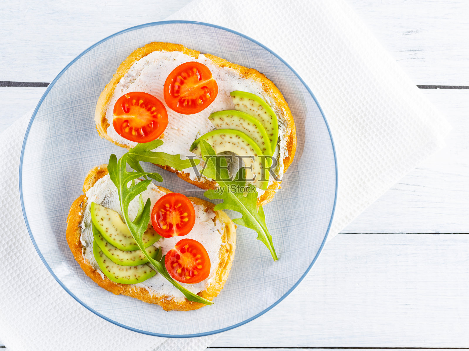 牛油果吐司配奶油芝士和樱桃番茄。两块涂着牛油果和芝麻菜的吐司放在白板上。副本的空间。俯视图照片摄影图片