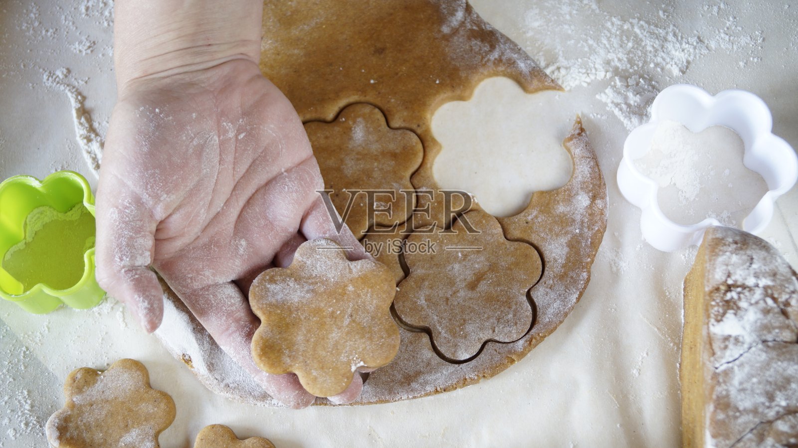姜饼面团躺在桌上。面团滚。剪出花朵的形状。手握相框照片摄影图片