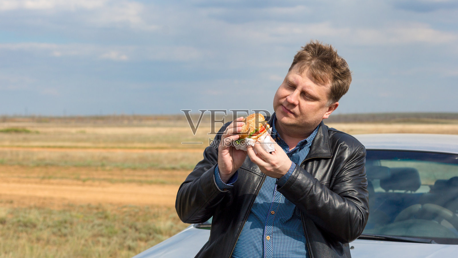 穿夹克的高个男人在草原上吃汽车照片摄影图片