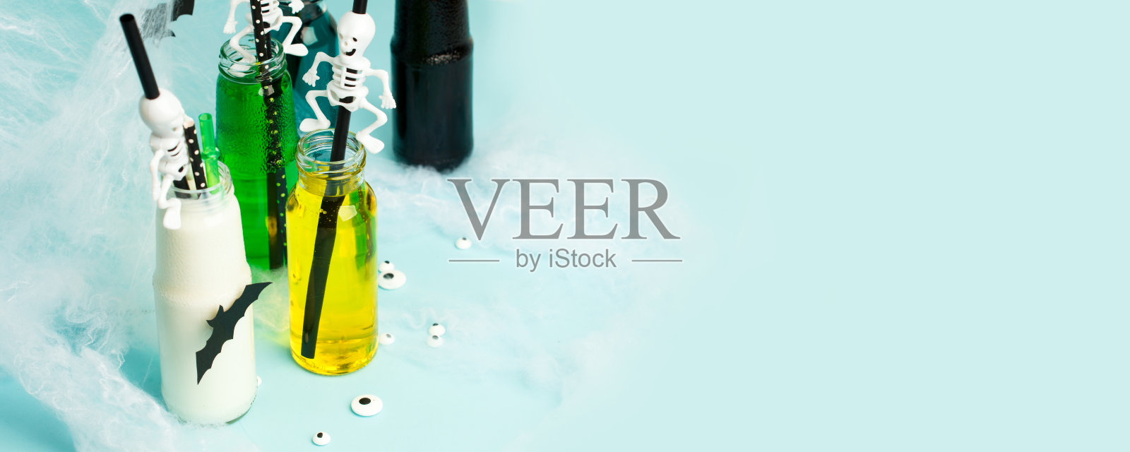 万圣节幽灵饮料，彩色鸡尾酒派对在玻璃瓶与令人毛骨悚然的装饰-蜘蛛网，骷髅稻草在蓝色的背景，明亮的传单，优惠券，横幅假日添加照片摄影图片