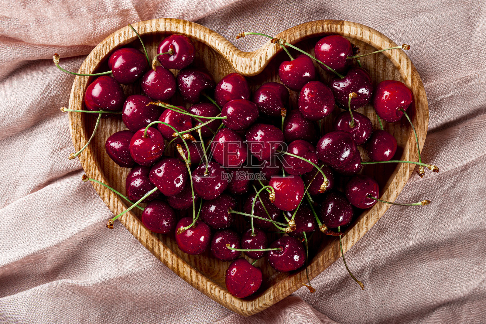 熟透的甜樱桃放在一个心形的木盘子上，粉红色的背景俯视图照片摄影图片