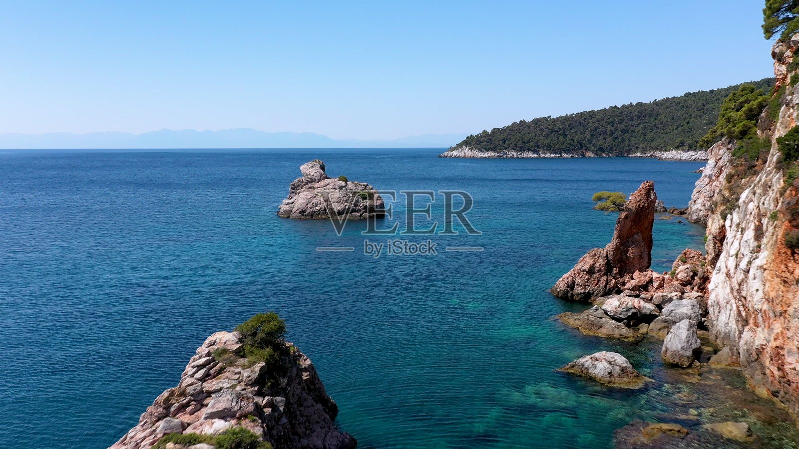 在希腊斯科佩洛斯岛，无人机俯瞰岩石嶙峋的海岸线、清澈的爱琴海水域、旅游海滩和大量的绿色植物。这是许多类似的希腊岛屿的典型景观。照片摄影图片