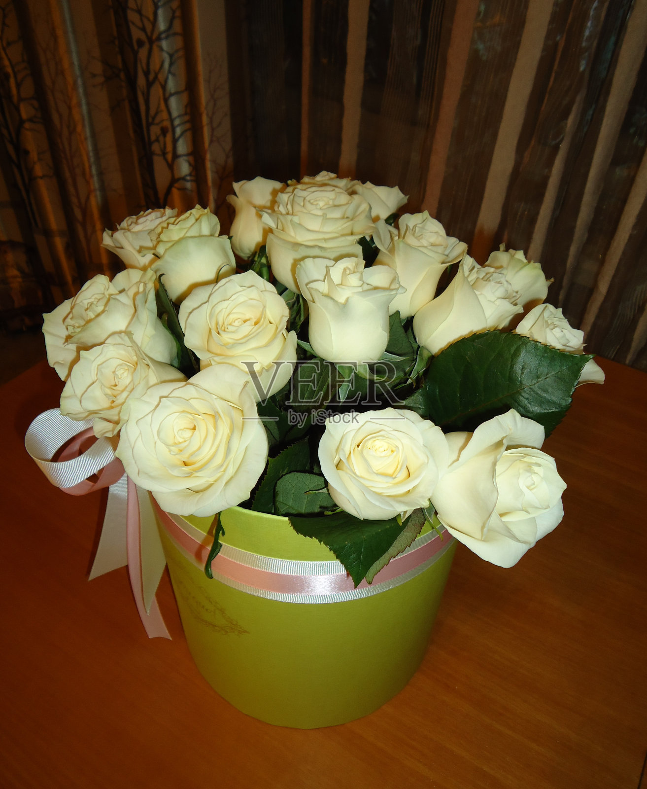 木桌上，绿桶里放着一束淡黄绿色的玫瑰，上面系着粉色和白色的丝带。桶的玫瑰。照片摄影图片