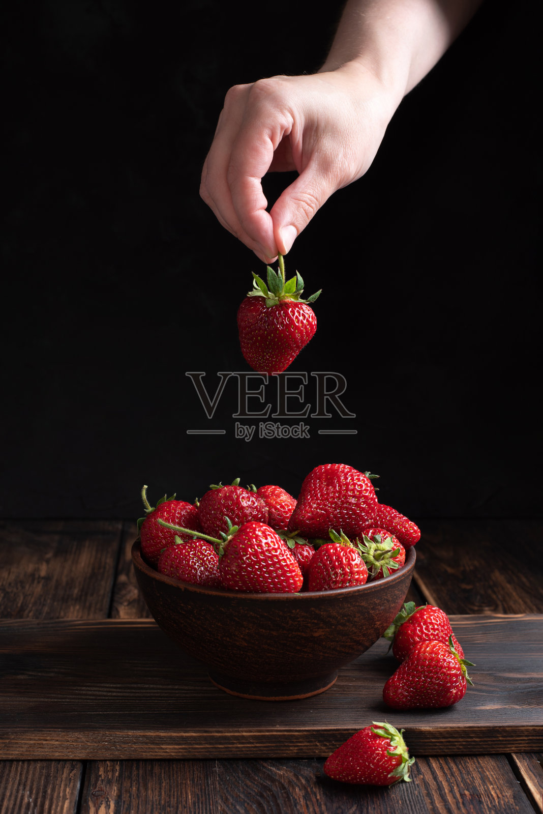 女性手把成熟的草莓放在一个碗里，草莓放在一个木制的背景上，乡村风格，夏天的概念。照片摄影图片