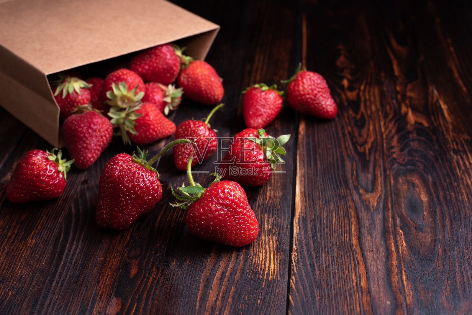 新鲜的草莓从纸袋里掉出来，黑色的木质背景，夏天的概念。照片摄影图片
