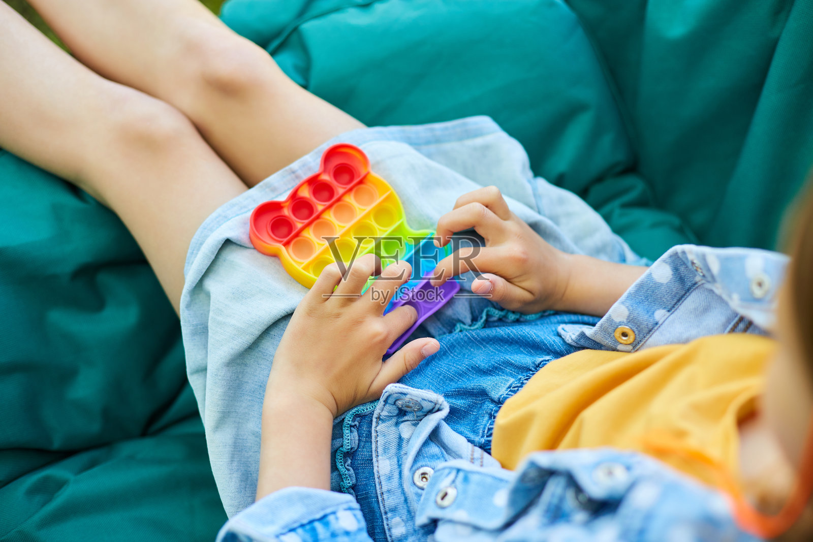 一个小女孩在户外的吊椅上玩pop it，小孩手里玩着五颜六色的pop it照片摄影图片