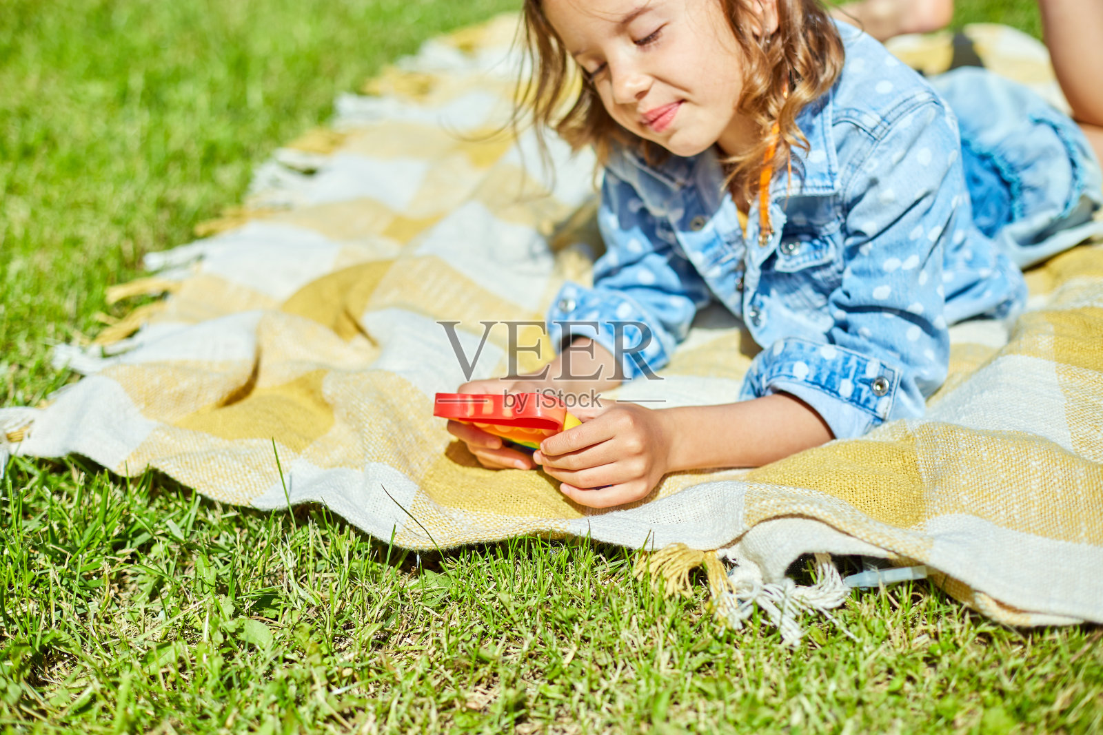 小女孩躺在毯子上在户外玩pop it，小孩的手上玩着五颜六色的pop it照片摄影图片