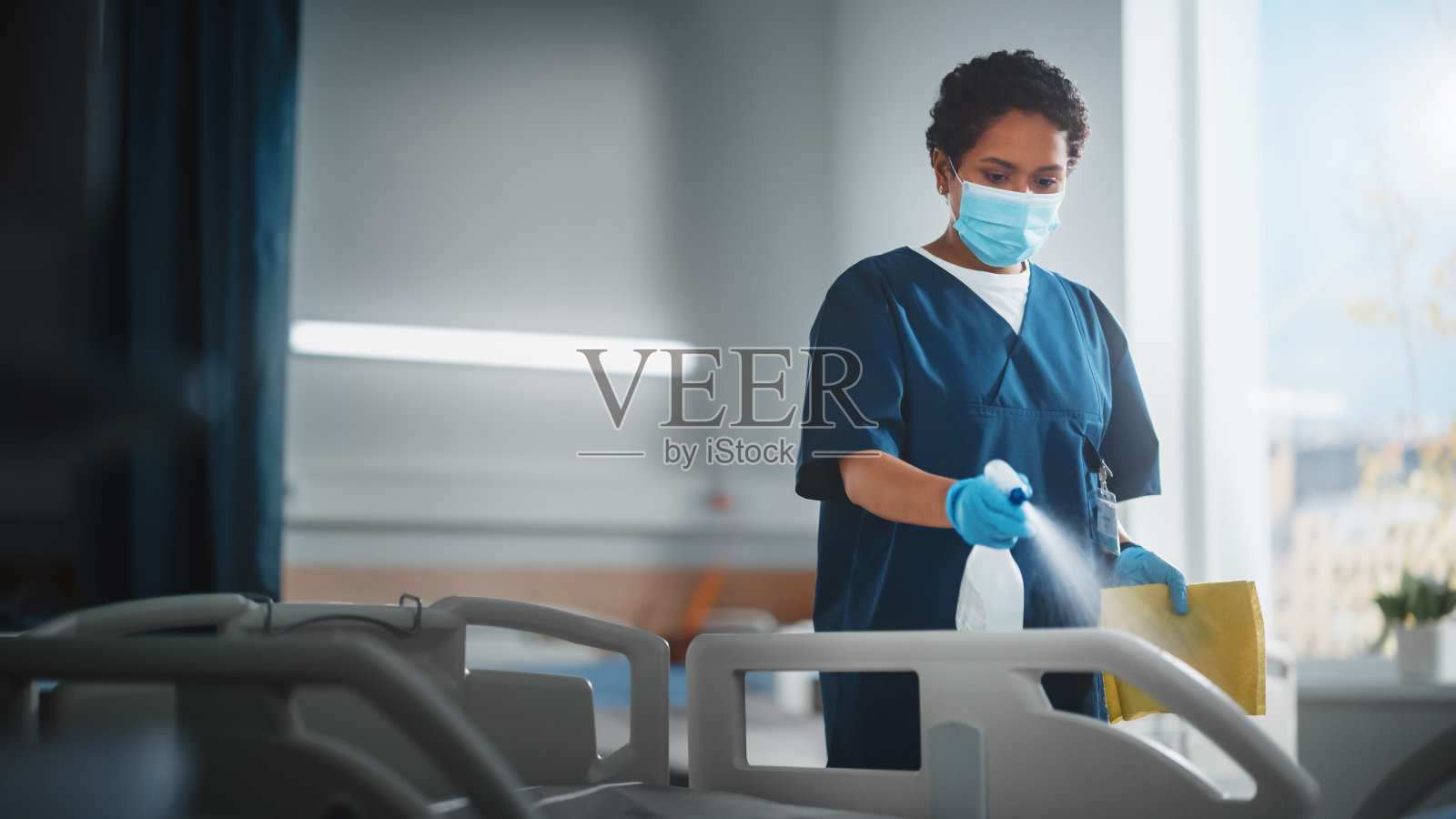病房:专业黑色护士戴口罩，擦拭床，Covid-19患者康复后清洁房间。冠状病毒感染者后的消毒、消毒、消毒诊所照片摄影图片