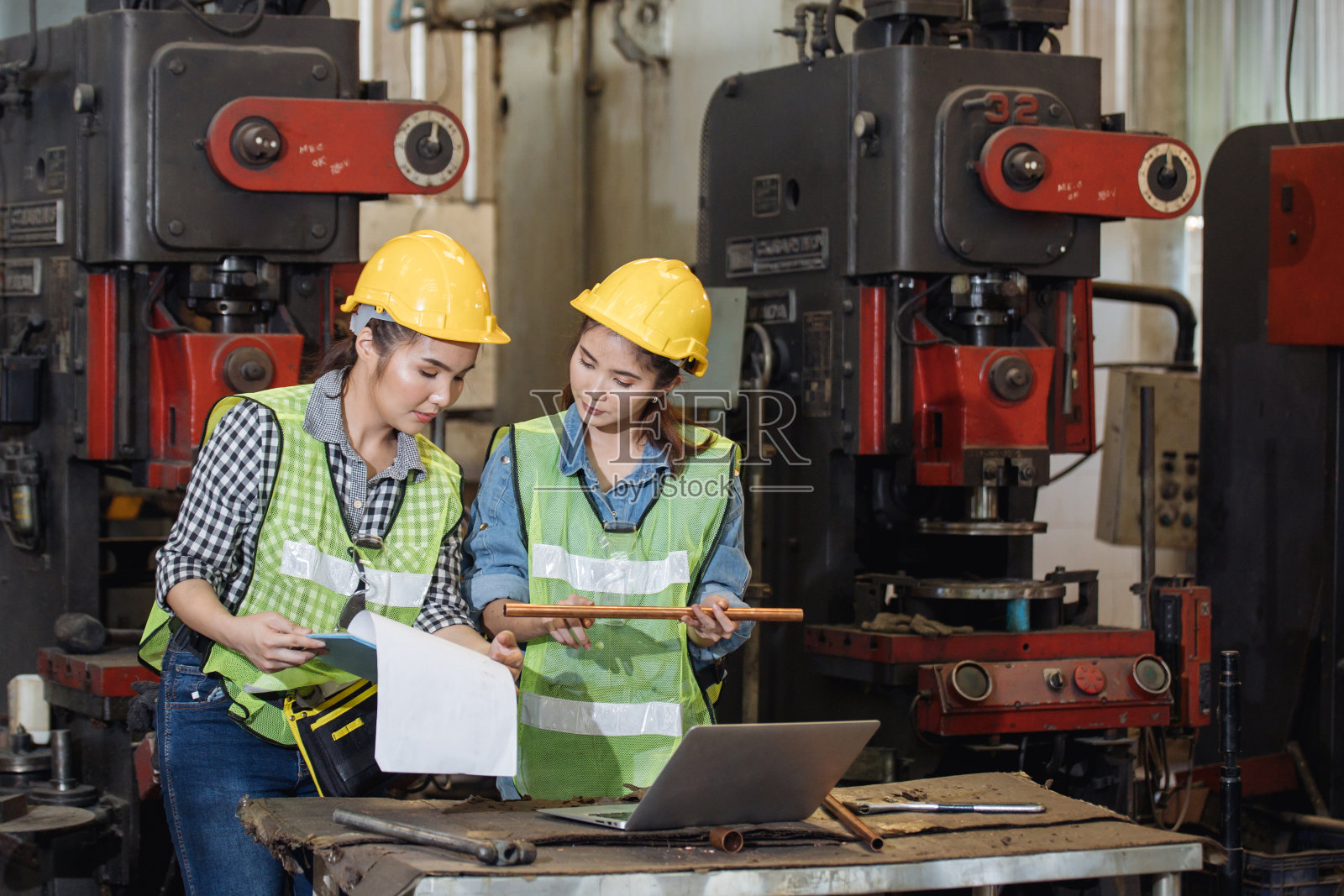 亚洲工程和工人妇女在安全安全帽和反光布使用车床在工厂内。一幅在工厂里拿着笔记本电脑的女工程师的肖像，照片摄影图片