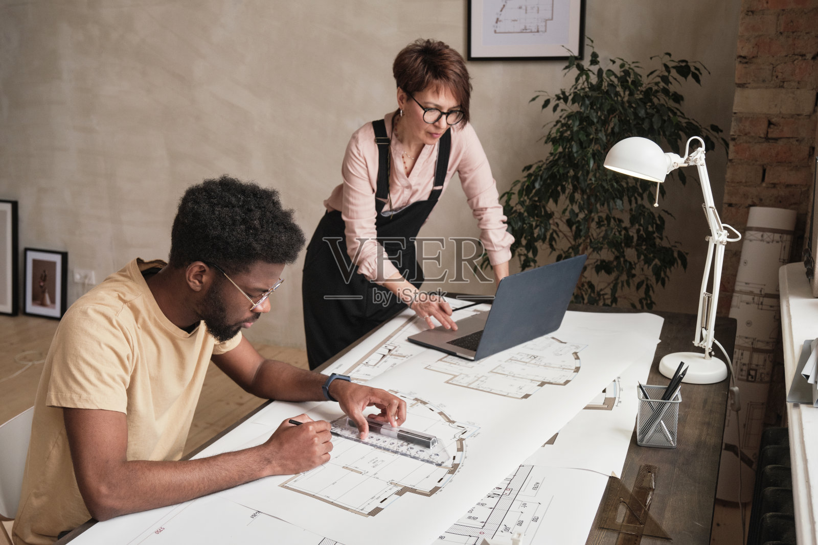 跨种族建筑员工在建筑项目工作，黑人绘制蓝图，而成熟的女士使用笔记本电脑照片摄影图片