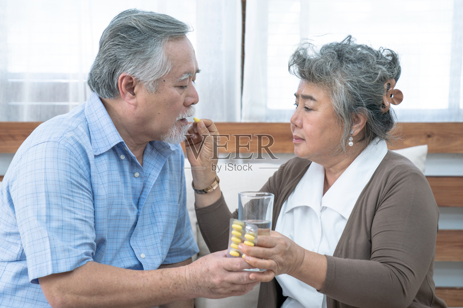 亚洲老夫妇，照顾退休后的健康，老年妇女在家帮助丈夫吃药或服用维生素片。照片摄影图片