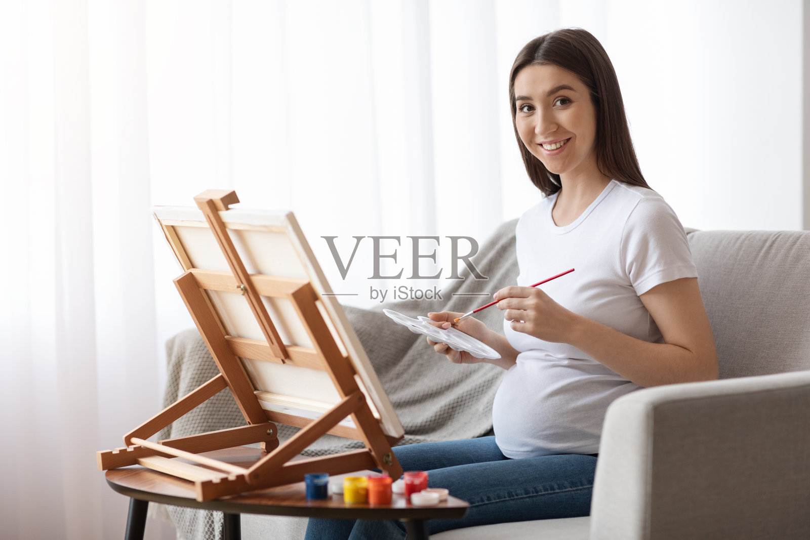 怀孕期间消遣。在家画架上画着美丽的孕妇照片摄影图片