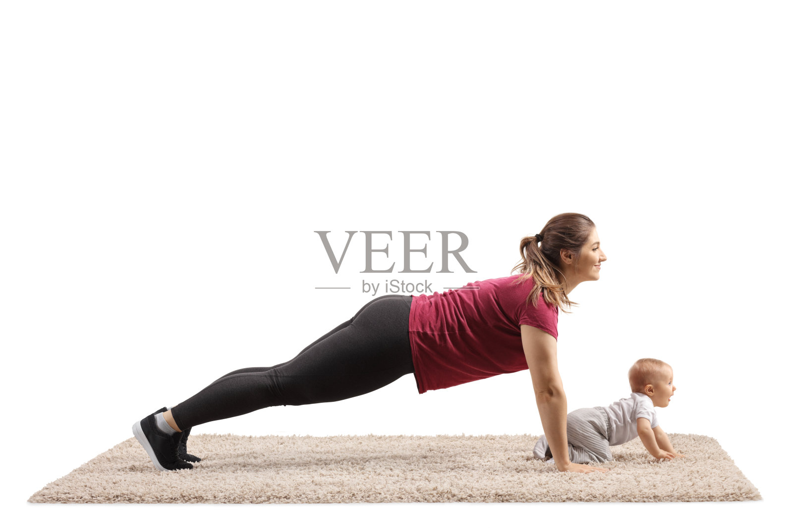 年轻的母亲做平板支撑练习，她的孩子在地毯上爬照片摄影图片