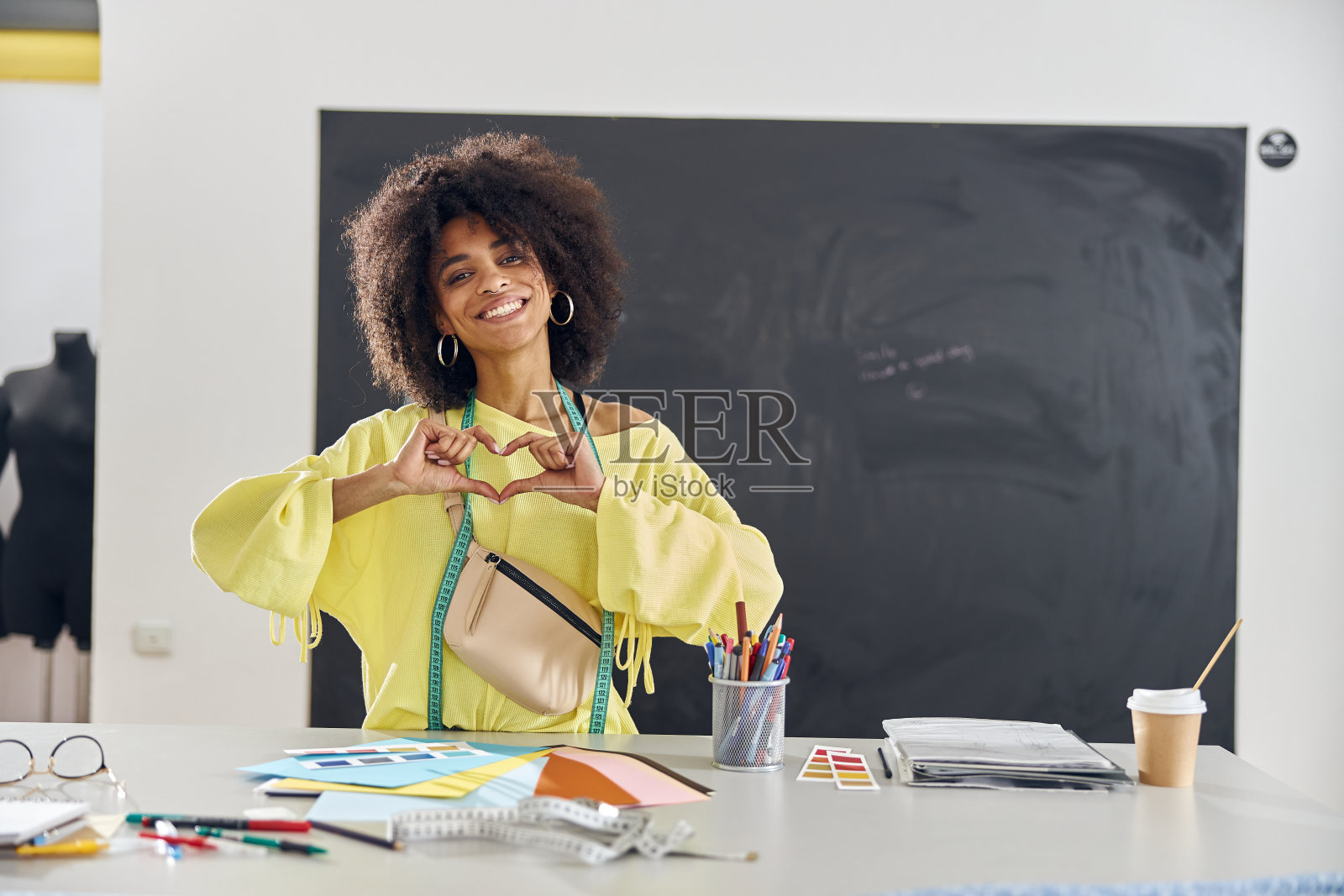 一位年轻的非洲裔美国家庭教师穿着亮黄色的毛衣，在缝纫课上用手指指点点照片摄影图片