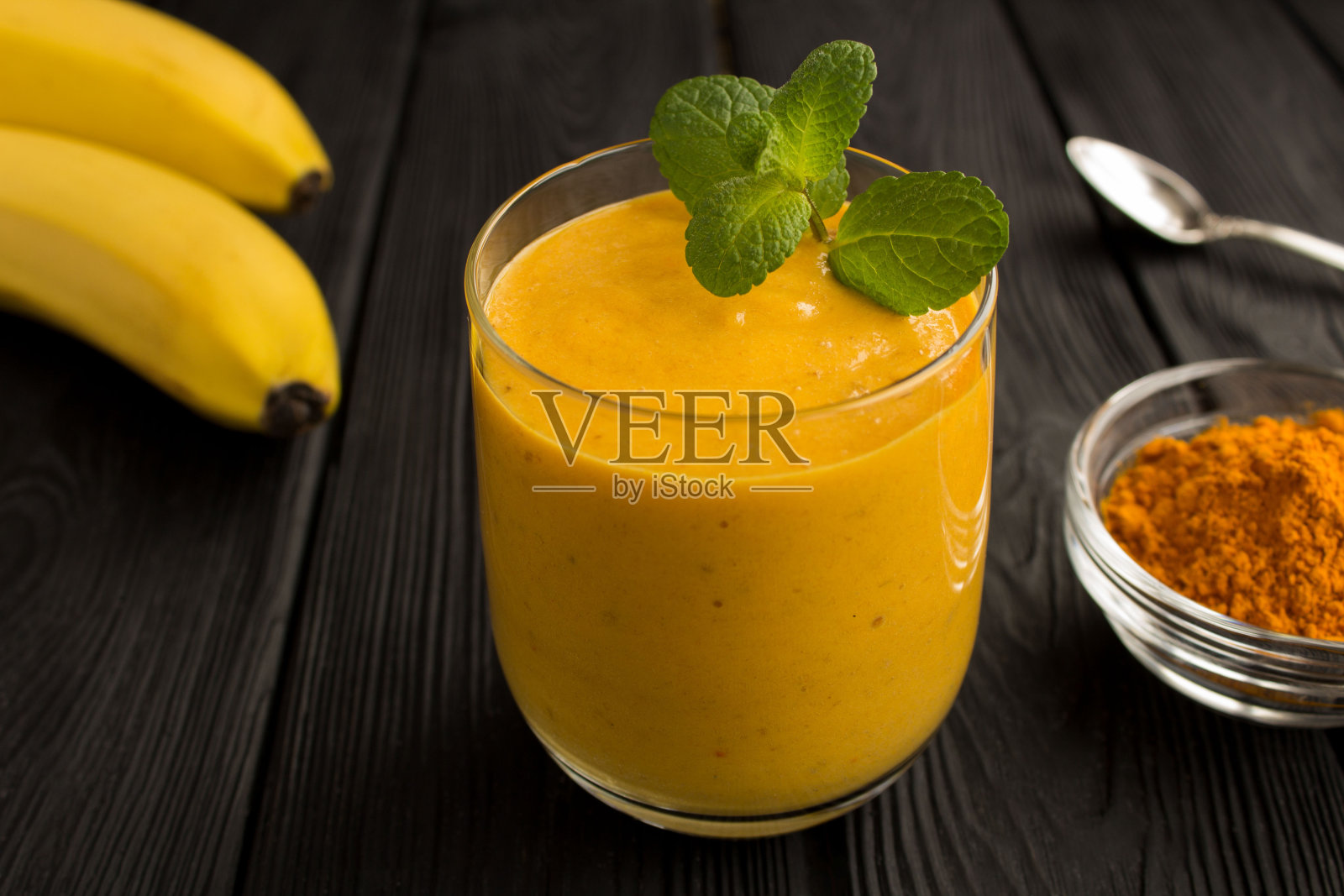 香蕉和姜黄冰沙在饮用玻璃上的黑色木制背景照片摄影图片