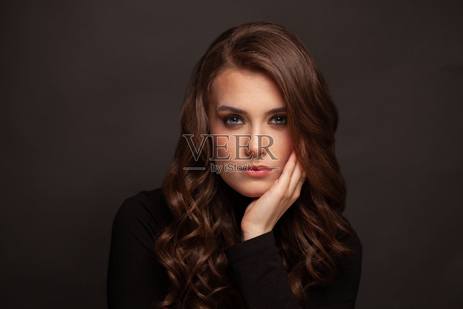 黑发女孩，长而有光泽的卷发。美丽的模型与卷曲的发型在黑暗的背景。照片摄影图片