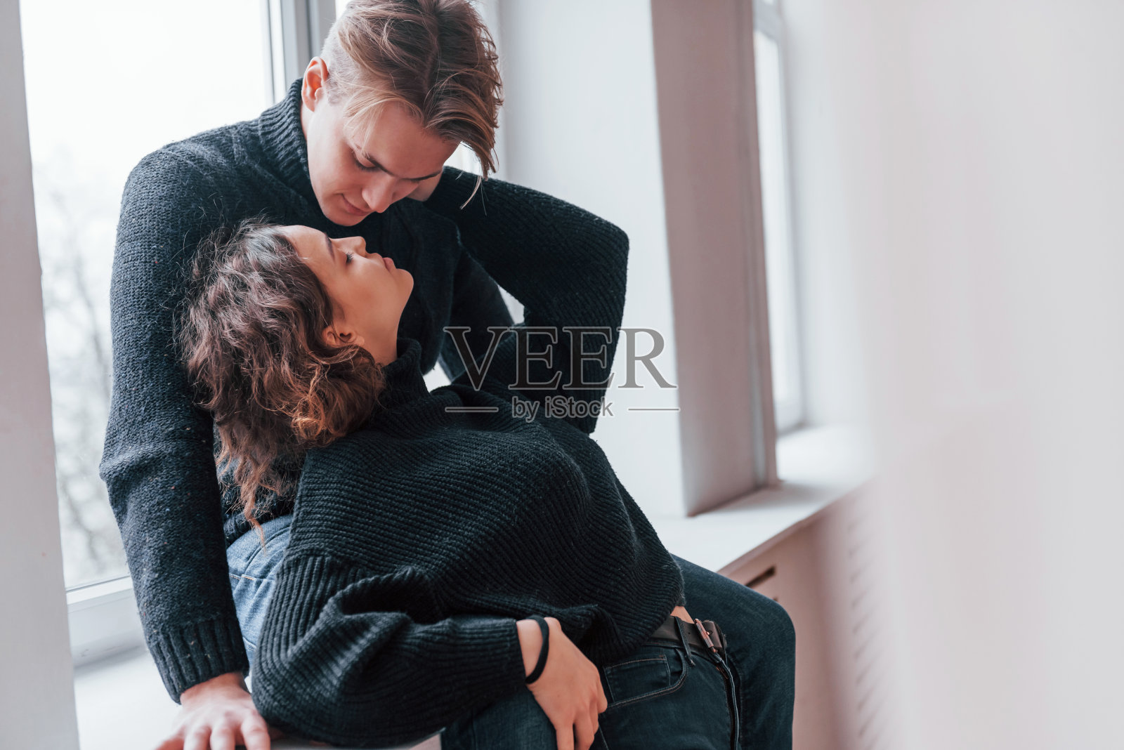 一对可爱的年轻夫妇在室内靠近窗户的地方互相亲吻照片摄影图片