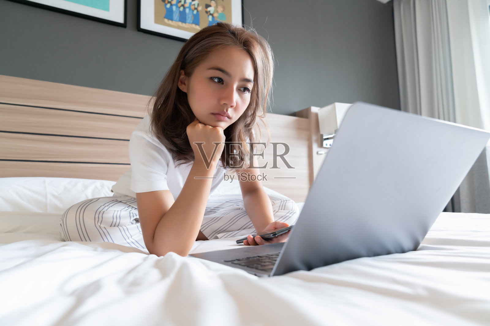 漂亮的亚洲女人躺着微笑着躺在床上和她的笔记本电脑。照片摄影图片