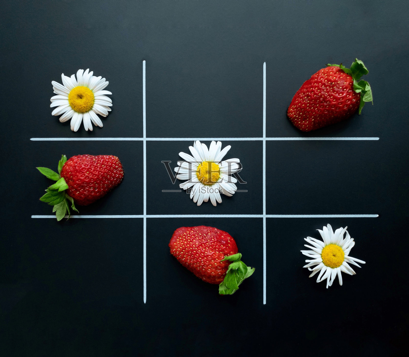 以洋甘菊和草莓为背景的井字游戏。平的。自然的概念。照片摄影图片