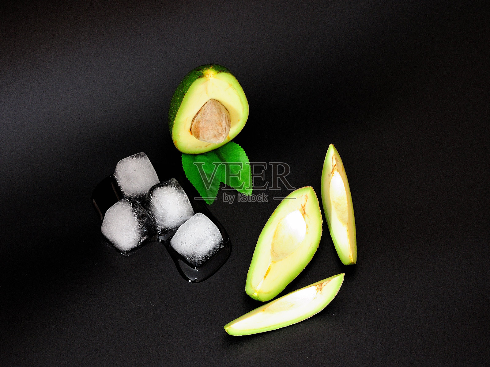 在黑色的背景上切好成熟的鳄梨和融化的冰块。照片摄影图片