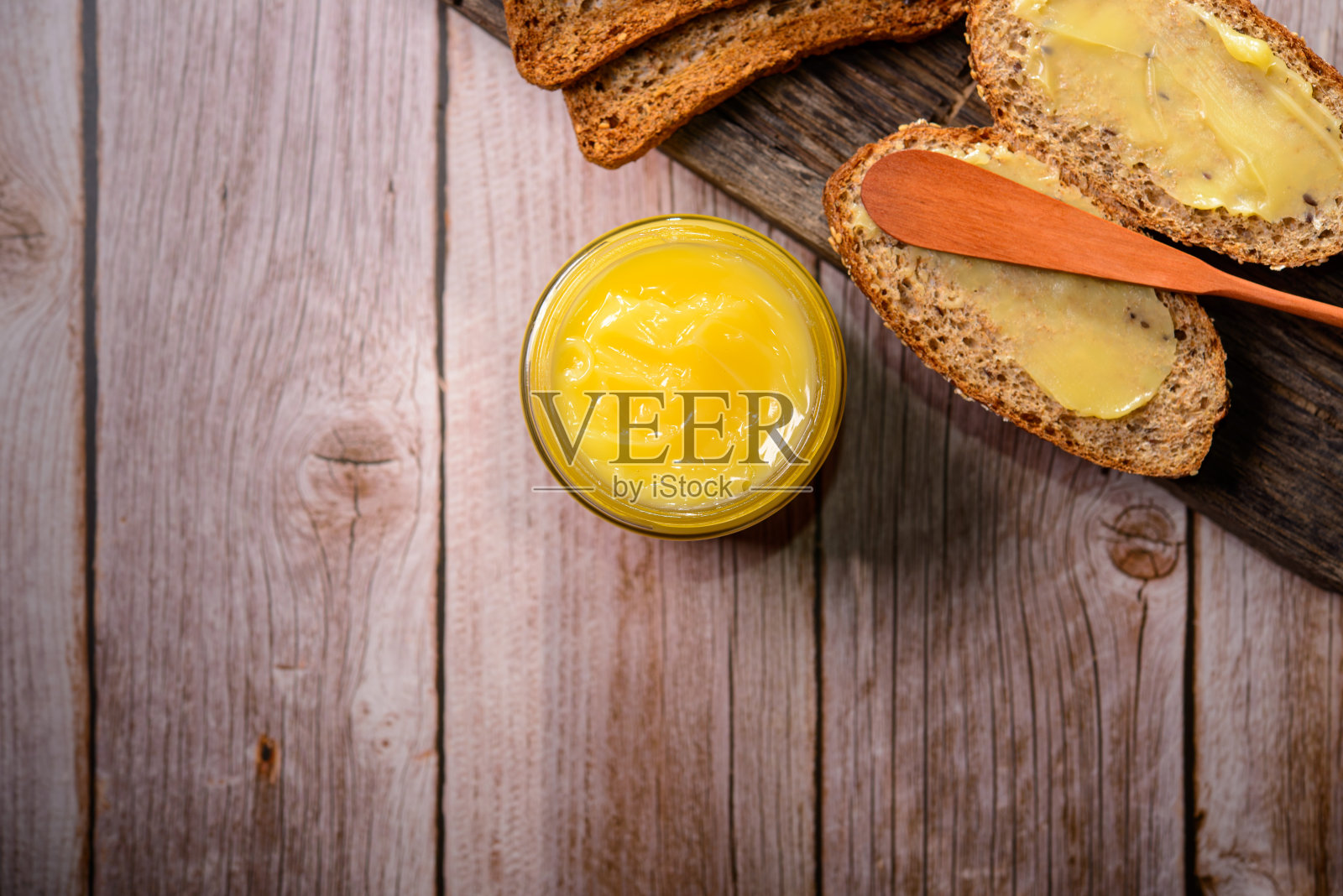 玻璃罐酥油和木制铲和切片面包在木桌上。照片摄影图片