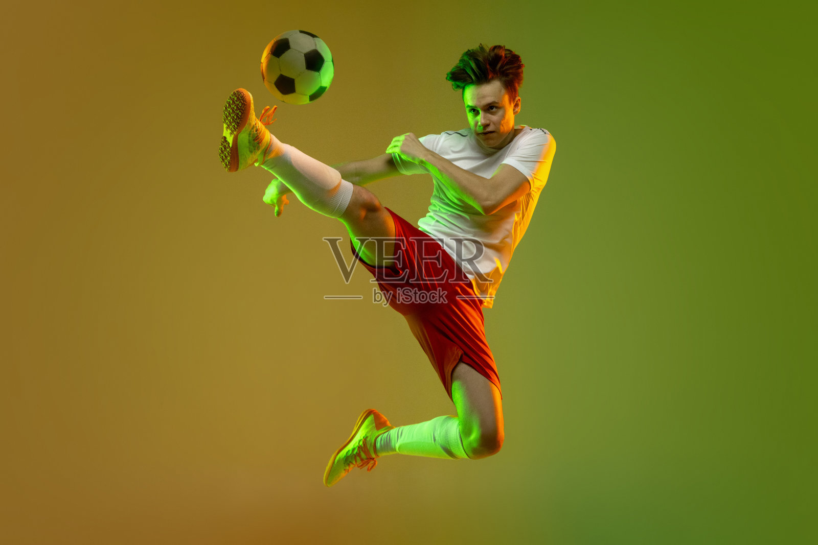 年轻的白人男子，男性足球运动员训练孤立在梯度黄绿色背景霓虹灯照片摄影图片